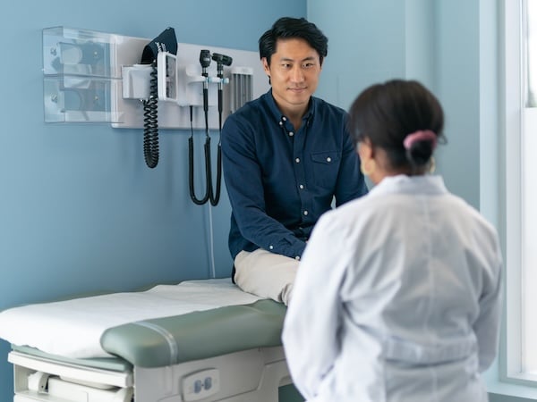 Man in consultation with doctor while sitting on treatment table in a physicians office. 