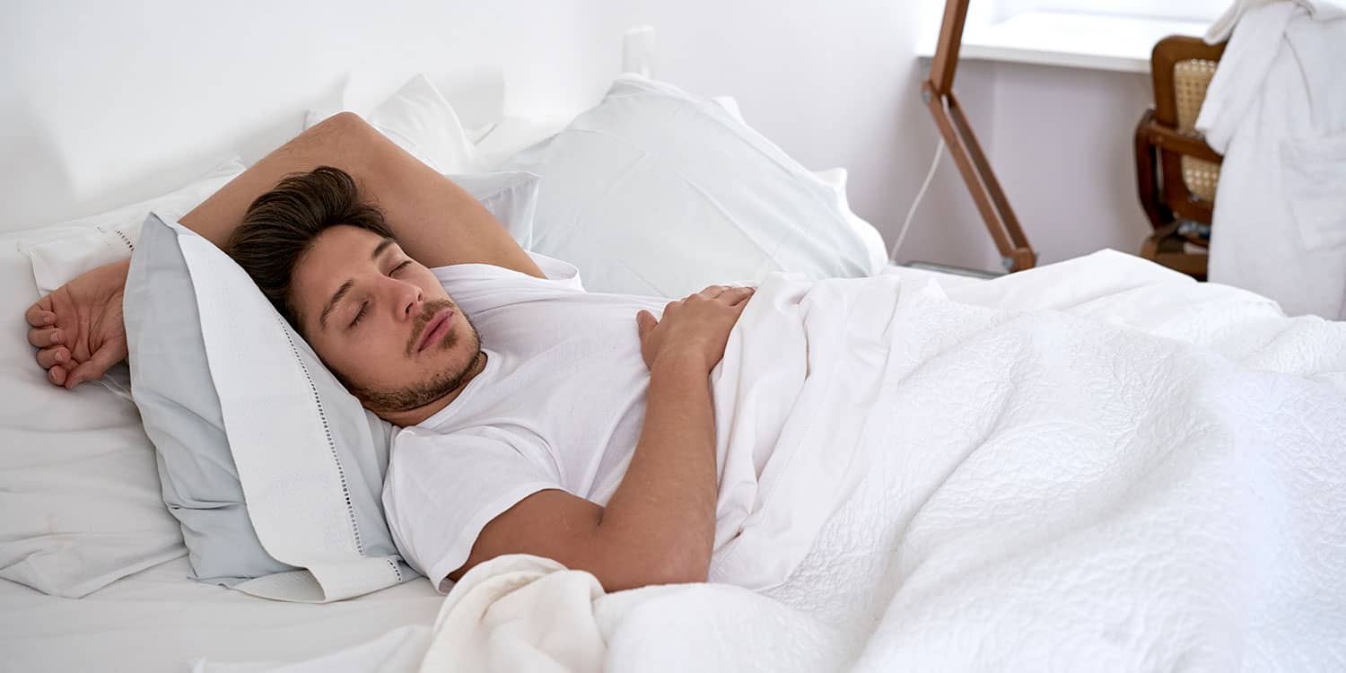 Man sleeping on his back in a bright bedroom with white bedding, supporting tips for better sleep